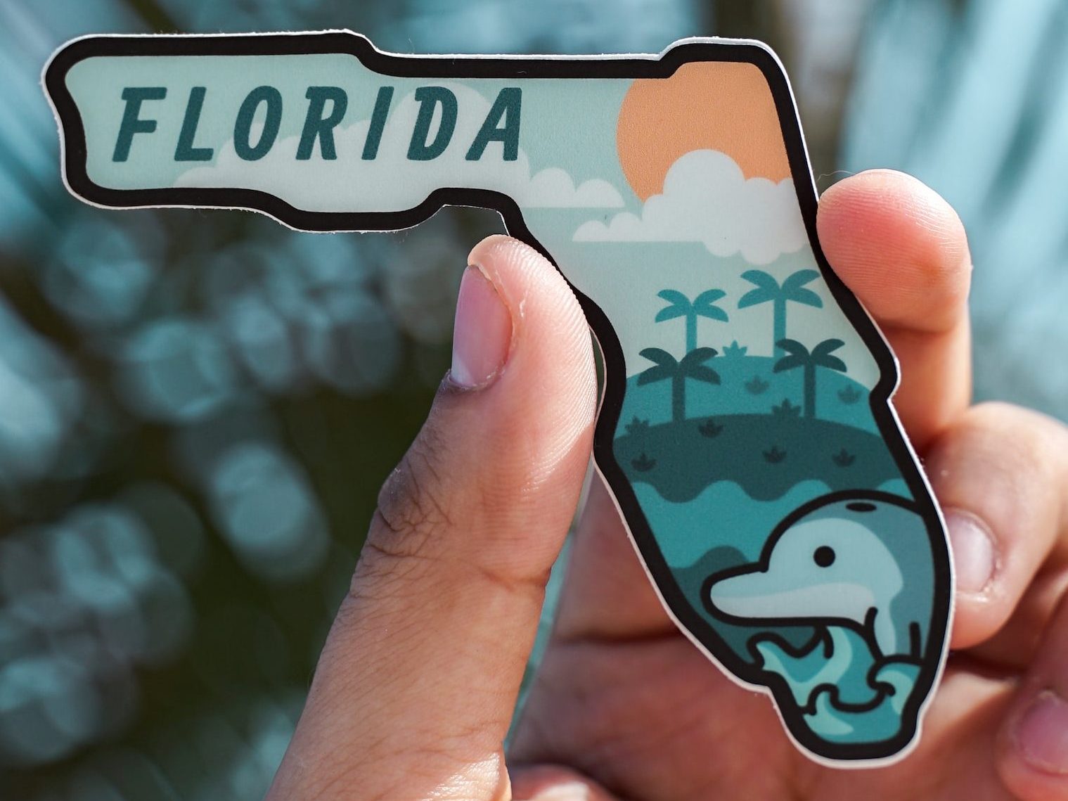 a man's fingers holding a florida shaped magnet