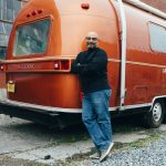man standing by rear bumper of red camping trailer