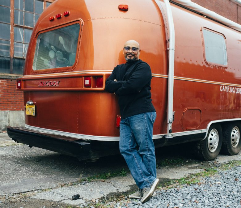 man standing by rear bumper of red camping trailer